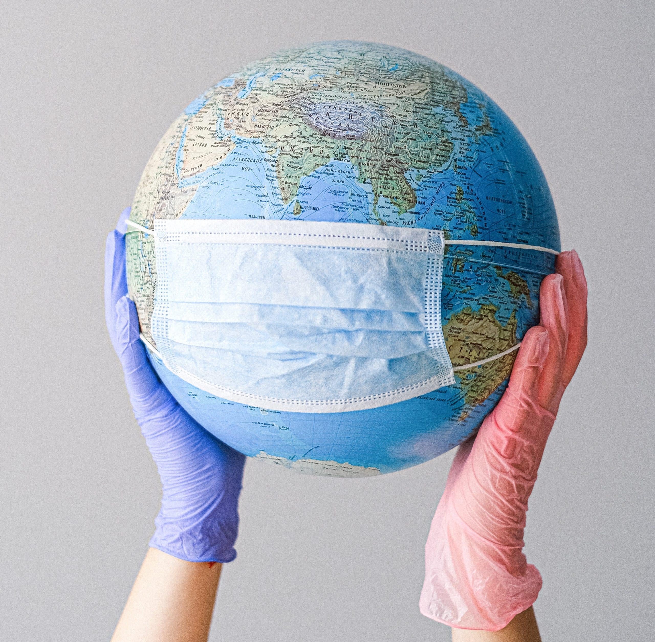 hands-with-latex-gloves-holding-a-globe-with-a-face-mask-